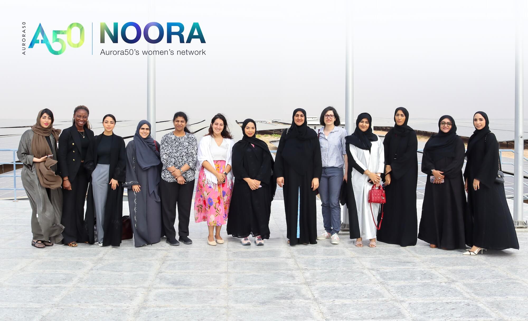 Members of Aurora50's GCC corporate women's network, NOORA, visit Noor solar park in Abu Dhabi on a site visit with founding partner TAQA in December 2024. Pictured 13 women standing in a row on a lookout platform with logo overlaid at top, Aurora50: NOORA - Aurora50's women's network.