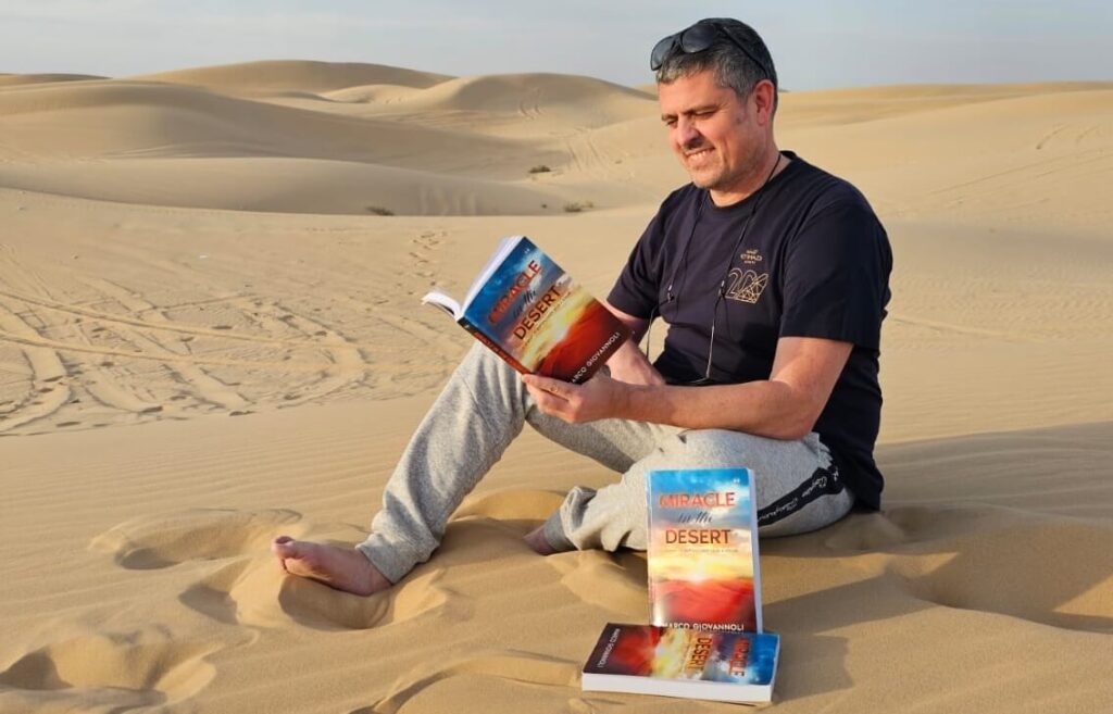 Marco Giovannoli, speaker at Aurora50's Inclusive Workplaces Summit 2024, in the desert with his book, Miracle in the Desert. Image supplied.