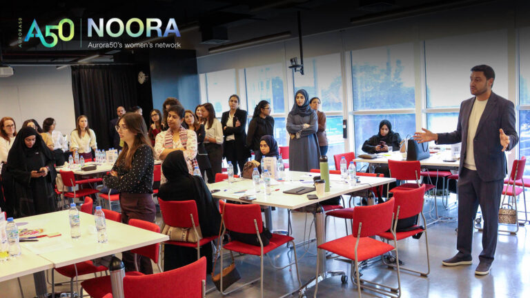 A photo from Aurora50's NOORA women's network (with logo) from a meet-up on 9 January 2025. The workshop focused on social capital and two male allies were invited to attend. In this photo, one man speaks while women gather.